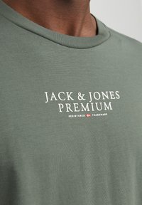 Žalias medvilnės marškinėliai su apvaliu iškirpimu, minkšta tekstūra ir balta spauda su užrašu „JACK & JONES PREMIUM“ priekyje.