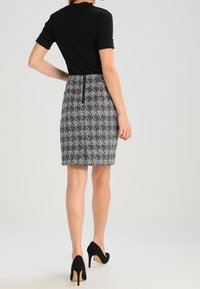 Atasan hitam lengan pendek dipadukan dengan rok hounds tooth ketat sepanjang lutut. Tampilan ini dilengkapi dengan sepatu hak tinggi hitam.
