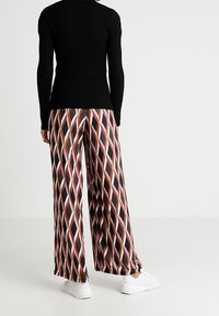 Haut noir à manches longues côtelé associé à un pantalon à jambes larges avec un motif en losange dans des couleurs chaudes et des baskets blanches.