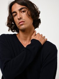 Marineblauer Strickpullover mit V-Ausschnitt, langen Ärmeln und weichem Textil, getragen von einer Person mit schulterlangem, lockigem Haar.