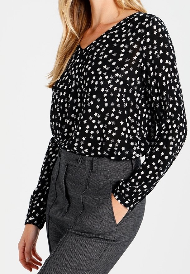 Blouse noire à motif d'étoiles blanches, col en V, manches longues, et tissu fluide ; assortie à un pantalon gris à motifs taille haute.