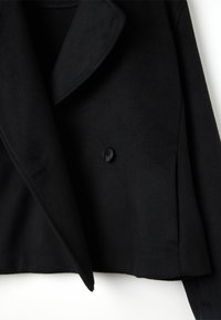 Giacca nera corta con ampi revers, chiusura con un bottone nero singolo e texture liscia. Design minimalista con bordi sartoriali.
