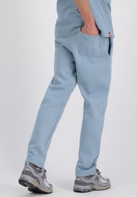 Lichtblauwe sweatpants van zacht materiaal met zijzakken en een comfortabele pasvorm, gecombineerd met grijze sportschoenen met meshaccenten.