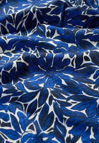 Bomullstyg med blå blommönster på vit bakgrund. Innehåller mörkblå blad och blommor, strukturerad yta och en flödande utseende.