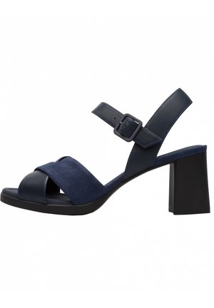 Granatowe sandały na wysokim obcasie z krzyżującymi się zamszowymi i skórzanymi paskami, regulowanym paskiem na kostkę z klamrą oraz solidnym czarnym obcasem w kształcie bloku.