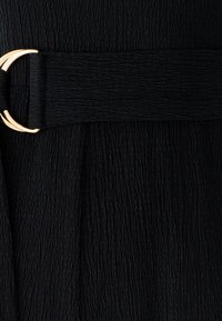 Black fabric with a textured surface, featuring a wide belt with a gold metallic buckle attaching it to the garment.