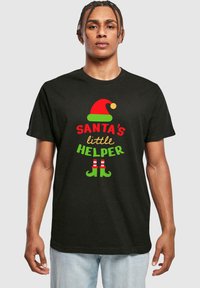 Tricou negru cu textul "MICUL AJUTOR AL LUI MOȘ CRĂCIUN" în culori roșii și verzi, însoțit de un grafic cu o pălărie de elf roșie și verde și pantofi în dungi. Mâneci scurte.