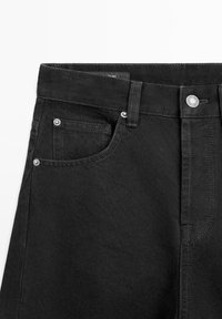 Schwarze Denim-Jeans im Taillenbereich mit sichtbaren Vordertaschen, Gürtelschlaufen, Knopfverschluss und Reißverschluss.