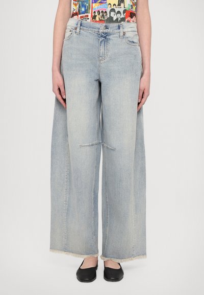 Jeans de denim cu picioare largi, de culoare bleu deschis, cu o margine brută, având o decolorare subtilă și o cusătură centrală. Asortați cu pantofi negri cu talpă joasă.