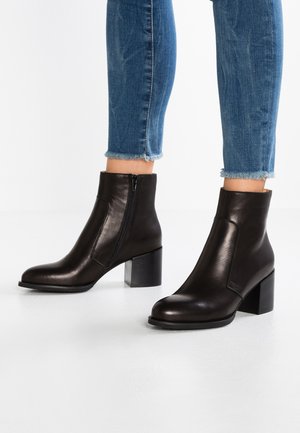 Kvinde iført sorte læderankelstøvler med blokhæle og sidelommer, parret med blå cropped jeans med frynset kant.