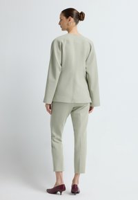 Jasnozielony, dopasowany garnitur z usztywnioną marynarką i wąskimi spodniami. Posiada długie rękawy, prosty krój i czysty szew na plecach. Burgundowe szpilki.