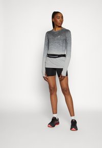 Langærmet, gradient grå atletisk top med sorte shorts. Har tommelfingerhuller og et sort talje bælte med et reflekterende bånd. Sorte løbesko.