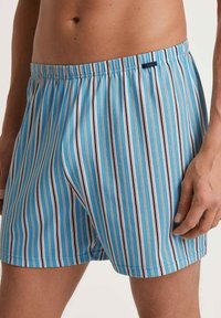 Boxers bleus à rayures avec une taille élastique, présentant des rayures verticales blanches, orange et marine. Tissu en coton lisse.