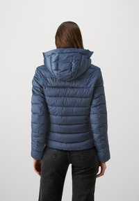 Giacca a vento imbottita blu navy con cuciture orizzontali, cappuccio e finitura liscia al tatto, caratterizzata da maniche aderenti e una forma leggermente sagomata.