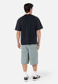 Black short-sleeve t-shirt with a relaxed fit, paired with light blue denim shorts. The model wears black and white sneakers with ankle socks.