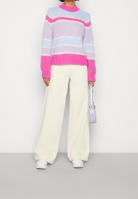 Chunky stickad tröja i pastellfärger som blått, rosa och lavendel med ribbade ärmslut och nederkant, parat med gräddvita vida byxor och vita sneakers.