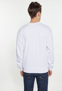 Hvid langærmet sweatshirt med runde halsudskæring, ribbede manchetter og en let afslappet pasform. Bæres med mørkeblå jeans.