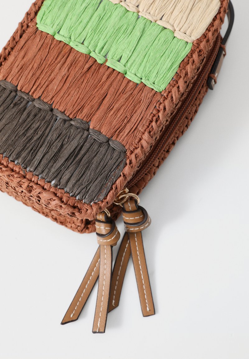 Bolsa tejida en secciones de marrón, verde, beige y negro. Presenta un material de paja texturizado, cierre de cremallera y borlas de cuero marrón.