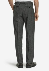 Pantalons à motif pied-de-poule gris avec une coupe ajustée, dotés de deux poches arrière et d'un pli à l'avant, associés à des chaussures noires.