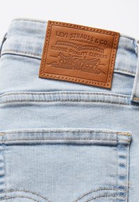Světle modré džíny z denimu s hnědou koženou etikou s nápisem "Levi Strauss & Co." a dekorativním prošíváním na zadních kapsách.