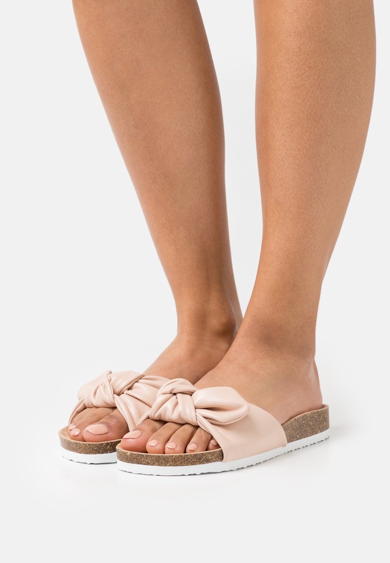 Sandales à glissière rose pâle avec un design noué, semelle en liège et semelle extérieure en caoutchouc blanc, présentant une texture lisse et un style à bout ouvert.