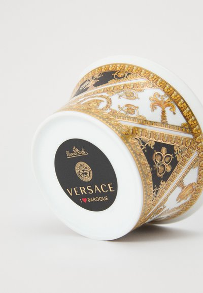Kerámia tál barokk mintákkal arany és fekete színekben, fényes fehér belsővel és egy fekete címkével, amelyen a Versace logó látható.