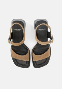 Μαύρα σανδάλια με τετράγωνη μύτη, με λουριά από ανοιχτό καφέ σουέτ και ασημί αγκράφες, με την επωνυμία Vagabond Shoemakers στην επιφάνεια του ποδιού.