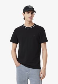 T-shirt in cotone nero con scollo bianco a costine, maniche corte e un piccolo logo nero sul petto. Abbinata a jeans denim azzurri.