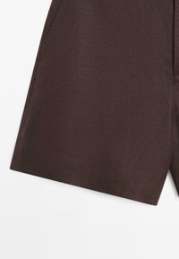 Brown linen shorts with visible side seam and front pocket edge on a white background.