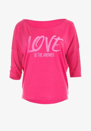 Rosa, löst sittande t-shirt med vid halsringning och trekvartslånga ärmar. Har en vit grafisk tryck med texten "KÄRLEK ÄR SVARET."