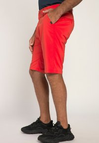 Rode shorts met een slim fit en een gladde textuur, voorzien van een knoop- en ritssluiting, en zakken. G gedragen met zwarte sport schoenen.