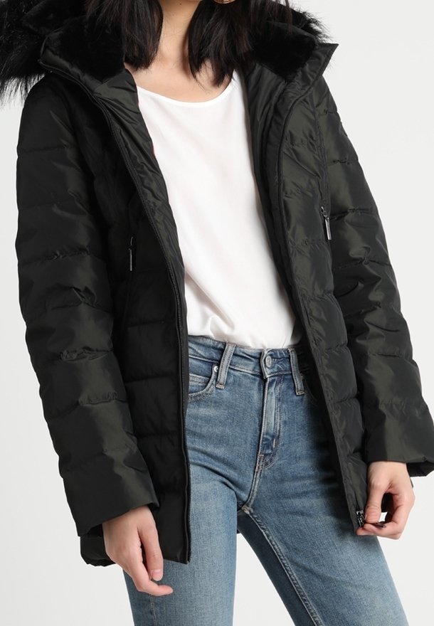 Sort dunjakke med hætte med imiteret pelskant, lynlåslommer og quiltet design, båret over en hvid skjorte og blå jeans.