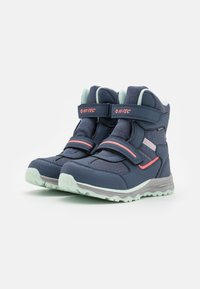 Marineblauwe hoge boots met klittenband, gaaspanelen en lichtgroene accenten. De rubberen zool heeft een gestructureerde grip voor tractie.