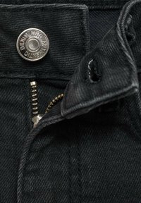 Črne jeans hlače iz denima z zaklepom na srebrni gumb, vidno zadrgo in trdno teksturo tkanine. Povečan pogled na detajle pasu.