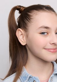 Złote kolczyki w kształcie liści z małymi akcentami kryształowymi, noszone przez osobę z długimi prostymi włosami w pół kucyku.