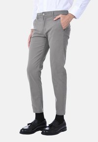 Pantaloni di cotone grigi con un design aderente, tasche frontali e una texture liscia, abbinati a mocassini neri e calzini.