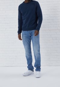 Felpa navy con maniche lunghe, collo a giro; abbinata a jeans azzurri chiari e sneakers bianche; vestibilità casual. Tessuto testurizzato, design semplice.