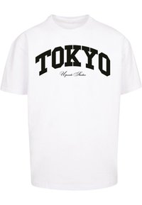Balta medvilnės marškinėliai su juodu kreipiamu "TOKYO" spaudiniu ir "Upscale Studios" mažu, elegantišku šriftu po juo. Trumpomis rankovėmis, laisvas kirpimas.