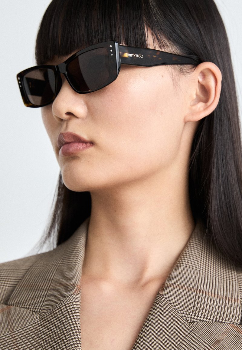 Zwarte zonnebril met een rechthoekig montuur, bruin getinte lenzen, zilveren accenten en het "Jimmy Choo"-logo op de donker tortoise-shell armen.