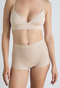 Set di reggiseno beige senza cuciture e pantaloni shorts a vita alta realizzati in tessuto morbido, caratterizzato da un design semplice con spalline sottili e senza parti metalliche visibili.