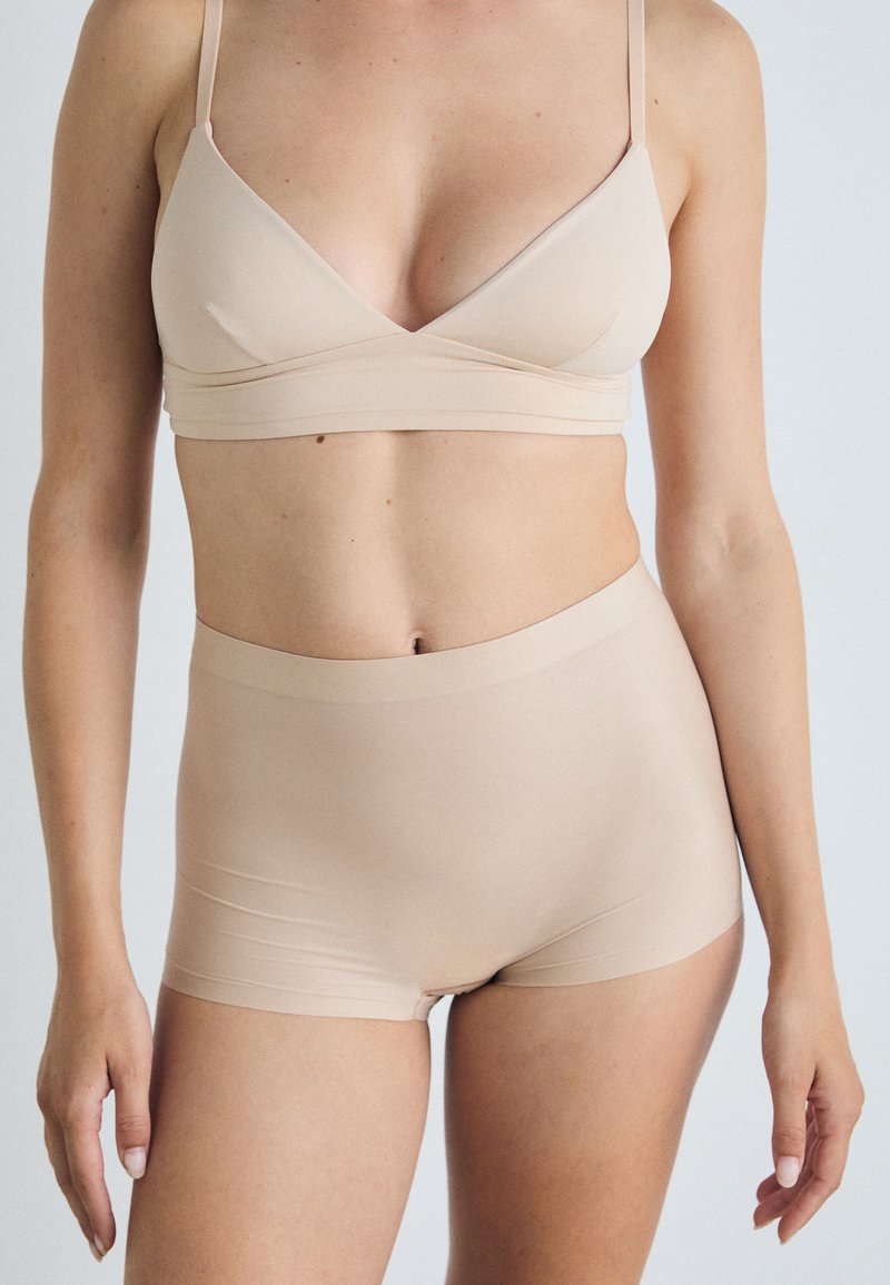 Set di reggiseno beige senza cuciture e pantaloni shorts a vita alta realizzati in tessuto morbido, caratterizzato da un design semplice con spalline sottili e senza parti metalliche visibili.