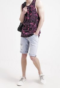Černý a fialový tie-dye tílko, světle modré deniminové šortky s roztrhanými okraji a bílé tenisky se šedými tkaničkami. Černá kabelka přes rameno.