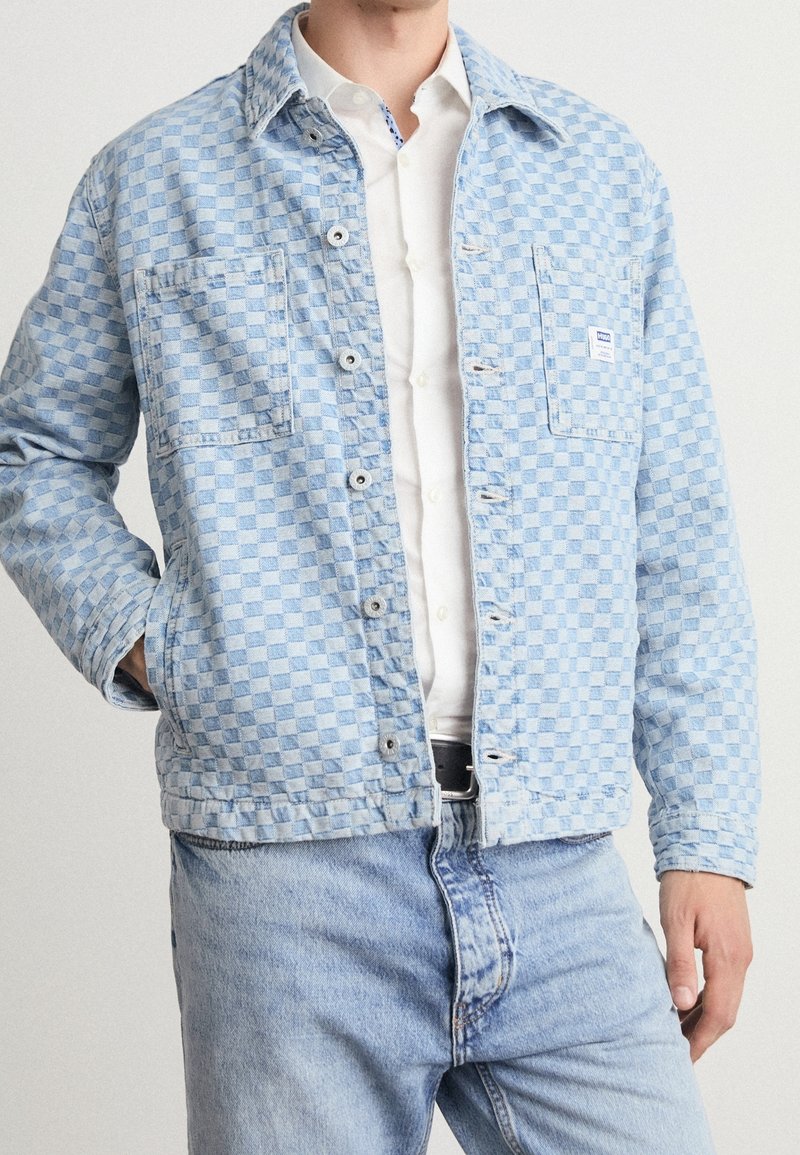Light blue checkered denim jacket featuring two front pockets, button closure, and a fold-down collar, paired with matching light blue jeans.