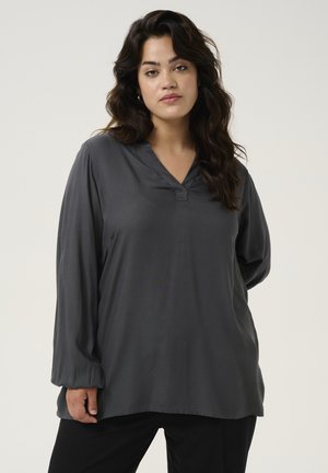 Blouse à manches longues gris foncé avec un décolleté en V, en matériau lisse. Comprend une patte de boutonnage discrète au niveau du cou et des manches légèrement froncées.