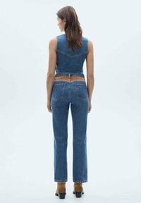 Denim brezrokavnik in komplet hlač z visokim pasom; temno modra, prilega se oblikovanju z rjavim pasom. Ima zadnja žepa in obliko hlač z razširjenim robom.
