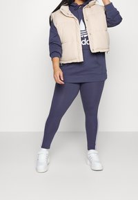 Laivastonsininen huppari, vaalean beige toppaliivi, laivastonsiniset leggingsit valkoisilla sivu-urilla ja valkoiset lenkkarit. Saumatonta kangasta.