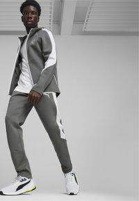Dres sportowy w kolorze szarym z białymi panelami bocznymi, składający się z kurtki na zamek i zwężających się spodni, uzupełniony białymi i czarnymi sneakersami.