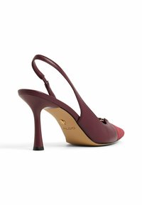 Burgunderfärgad slingback-högklackad sko med spetsig tå, i mocka och lädermaterial, samt en smal klack. Har en guldfärgad logo på innersulan.