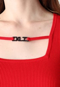Rotes geripptes Oberteil mit einem schwarzen Metallverschluss, auf dem die Buchstaben "DKL" am Ausschnitt stehen, aus weichem Material und mit tailliertem Schnitt.