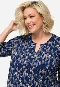 Granatowa koszula z geometrycznymi kremowymi wzorami, okrągłym dekoltem i rękawami do łokci. Materiał wydaje się miękki i teksturowany.